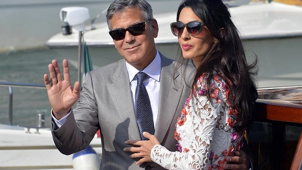 Aktor asal Amerika Serikat, George Clooney dan istrinya Amal Alamuddin melambaikan tangan ke arah awak media di atas taksi air saat melintas Grand Canal, Venice, Italia, Minggu, 28 September 2014.