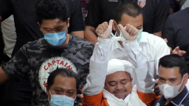 Rizieq Shihab (tengah) yang memakai baju tahanan dan tangan terborgol menuju mobil tahanan seusai menjalani pemeriksaan di Dirkrimum Polda Metro Jaya, Jakarta, Minggu 13 Desember 2020 dini hari.