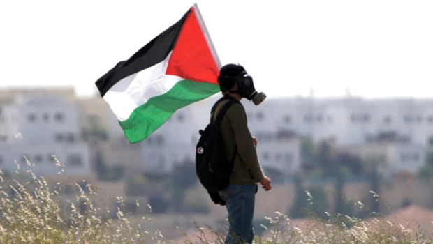 Seorang pemuda yang mengenakan masker gas dan memegang bendera Palestina terlihat saat bentrokan antara tentara Israel dan aktivis Palestina di sepanjang tembok pemisah kontroversial yang dibangun Israel. 