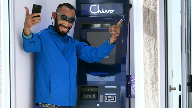 Seorang pria dengan masker bergambar Presiden El Salvador Nayib Bukele berpose di depan sebuah ATM bitcoin setelah aplikasi Chivo Wallet tidak bisa diakses di kota San Salvador, 7 September 2021.