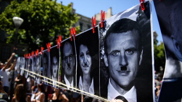 Para pengunjuk rasa menunjukkan spanduk yang menggambarkan wajah politisi, termasuk Presiden Emmanuel Macron, dengan kumis Hitler saat demonstrasi menentang langkah-langkah keamanan virus corona baru di Marseille pada 17 Juli 2021. 