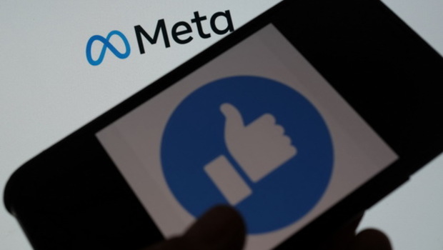 Seseorang menggunakan Facebook di smartphone di depan layar komputer yang menunjukkan logo META pada Kamis 28 Oktober 2021. Kepala Facebook Mark Zuckerberg mengumumkan nama perusahaan induk sedang diubah menjadi 