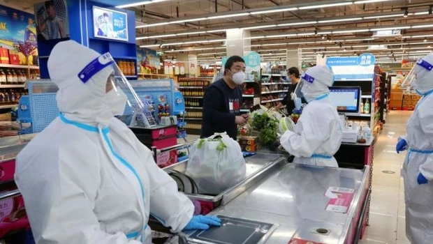 Pekerja dengan pakaian pelindung melayani pelanggan di konter kasir toko swalayan yang dibuka kembali, di tengah wabah Covid-19, di Shanghai, Tiongkok.