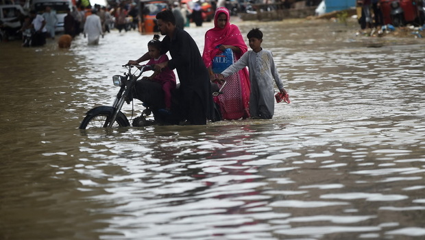 Satu keluarga mengarungi jalan yang tergenang banjir setelah hujan deras di Karachi, Pakistan pada Minggu 11 Juli 2022. 