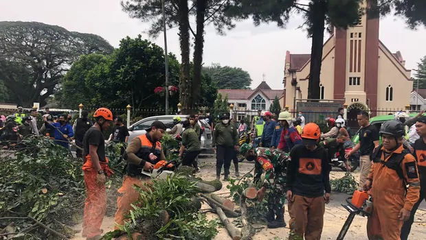 Sejumlah petugas memotong pohon yang tumbang di di depan GPIB Zebaoth, tak jauh dari Istana Bogor, Minggu sore (17/7/2022).