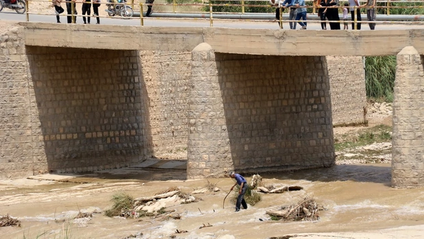 Orang-orang berdiri di jembatan di atas sungai, setelah banjir yang disebabkan oleh hujan lebat di daerah Estahban Iran selatan, yang dilaporkan menewaskan sedikitnya 21 orang pada Sabtu 23 Juli 2022.