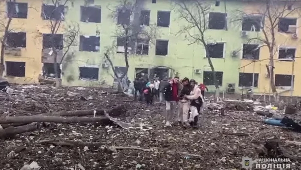 Orang-orang dibantu keluar dari bangunan rumah sakit anak-anak yang rusak setelah serangan udara Rusia di kota tenggara Mariupol pada Maret 2022.