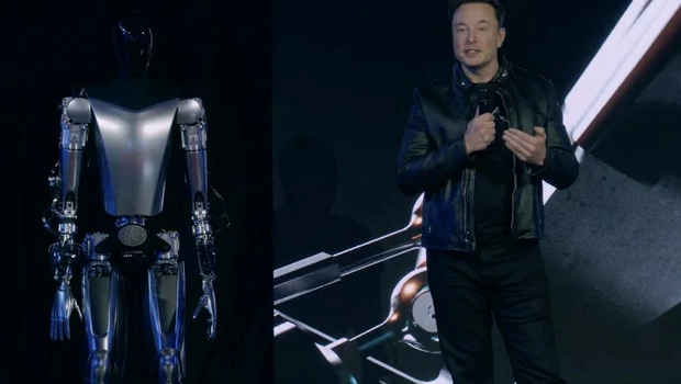 Tangkapan layar video yang dibuat dari siaran langsung Tesla AI Day 2022 ini menunjukkan Elon Musk berdiri di atas panggung di samping Optimus, robot humanoid di Palo Alto, California pada 30 September 2022.