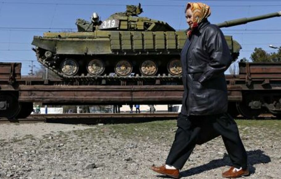 Seorang wanita berjalan melewati kereta api yang membawa tank Ukrania keluar dari wilayah Crimea.