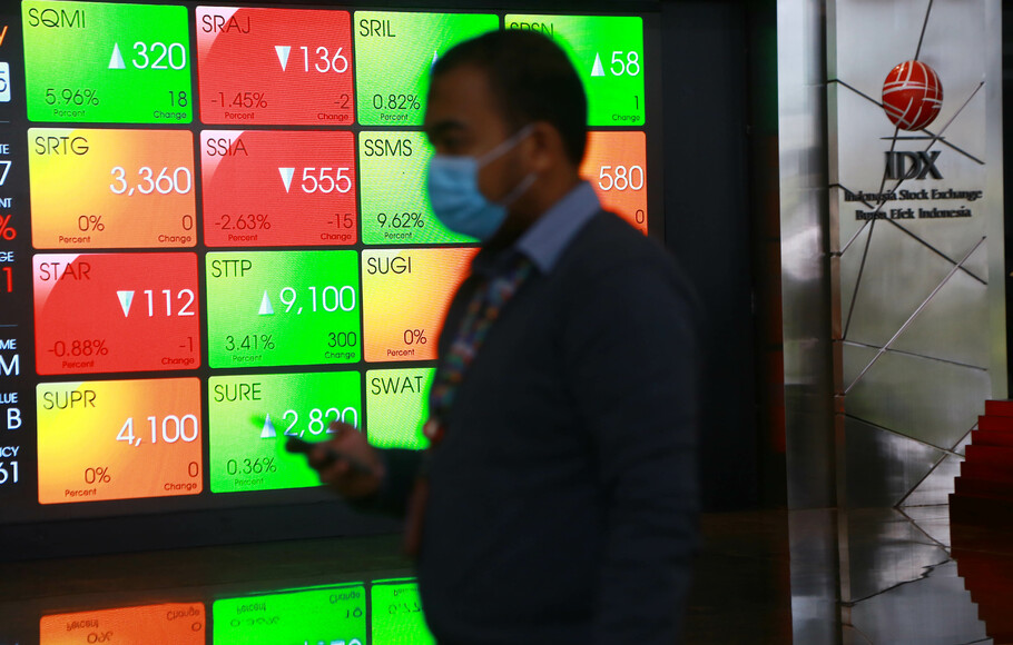 Karyawan berjalan di dekat layar monitor pergerakan harga saham di Jakarta.