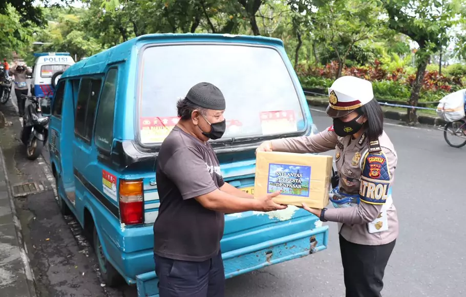Seorang polwan dari Satuan lalu Lintas (Satlantas) Polresta Denpasar, Bali, membagikan sembako kepada sopir angkot yang terdampak Covid-19, Rabu, 10 Februari 2021.