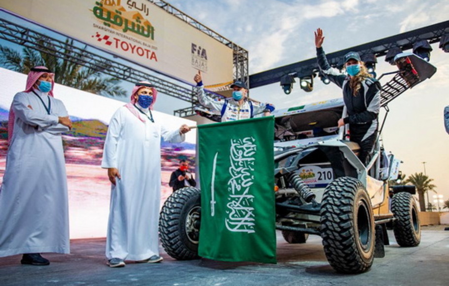 Pembalap Saudi Dania Akeel, wanita Saudi pertama yang mengikuti reli internasional, melambai di samping kendaraannya di Arab Saudi, Kamis (4/3/2021). Saudi mencabut sejumlah aturan pembatasan Covid-19 pada Minggu (7/3/2021). 