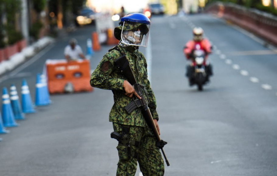 Foto yang diambil pada 25 Maret 2020 menunjukkan 
Seorang polisi mengenakan masker dan aparat berjaga di pos pemeriksaan setelah pemerintah memberlakukan karantina yang ditingkatkan sebagai tindakan pencegahan terhadap virus corona baru atau Covid-19 di Manila, Filipina, Kamis 25 Maret 2021. 