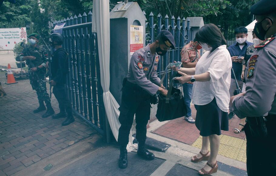 Personel polisi memeriksa barang bawaan umat didepan gerbang, jelang pelaksanaan misa kamis putih di  gereja Katedral Jakarta, Kamis 1 April 2021 sore.