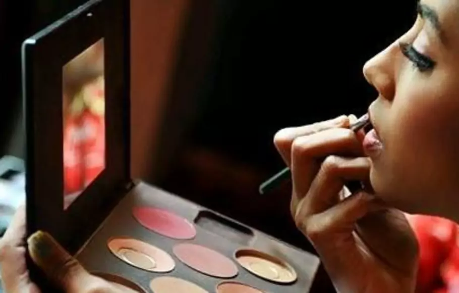 Wanita sedang menggunakan produk kosmetik untuk mempercantik wajahnya.  