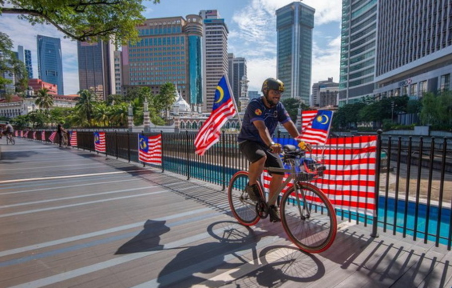 Seorang warga mengendarai sepeda dengan bendera nasional Malaysia untuk merayakan hari ulang tahun ke-64 kemerdekaan Malaysia di Kuala Lumpur, Malaysia, pada Selasa 31 Agustus 2021. 