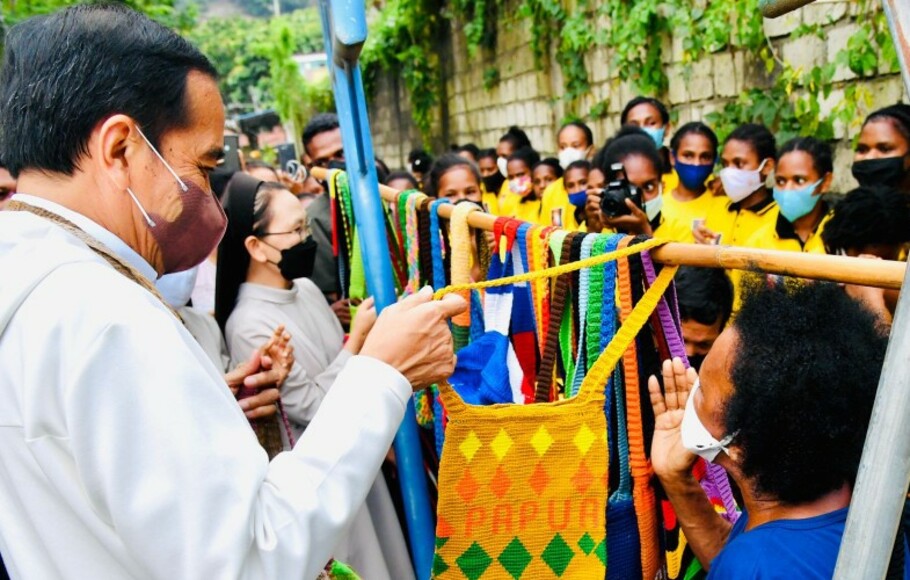 Presiden Joko Widodo (kiri) membeli tas rajutan asli Papua atau Noken, dari Mama-Mama penjual di Jalan Raya Hawai Sentani, Jayapura, Papua, Jumat, 1 Oktober 2021.  