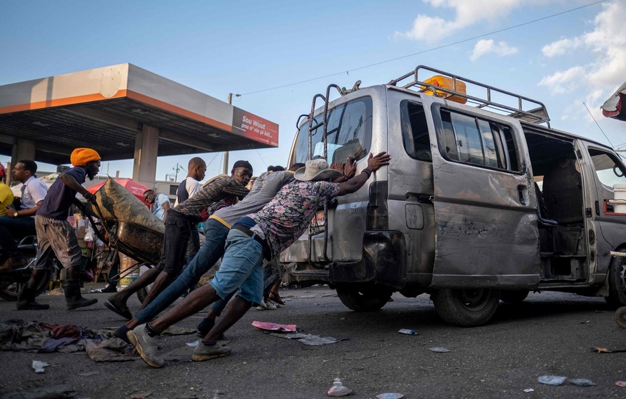 foto yang diambil pada 29 Oktober 2021 memperlihatkan, orang-orang mendorong mobil angkutan umum yang kehabisan bahan bakar di depan sebuah pompa bensin yang ditutup di Port-au-Prince, Haiti.
