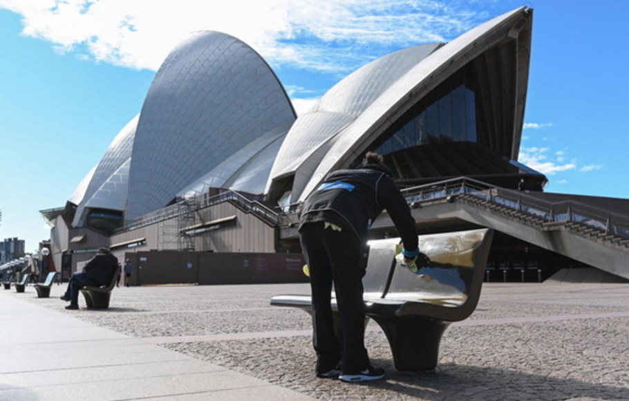 Seorang pekerja membersihkan tempat duduk umum di luar Gedung Opera di Sydney pada 26 Juni 2021, setelah pihak berwenang mengarantina beberapa area pusat kota.