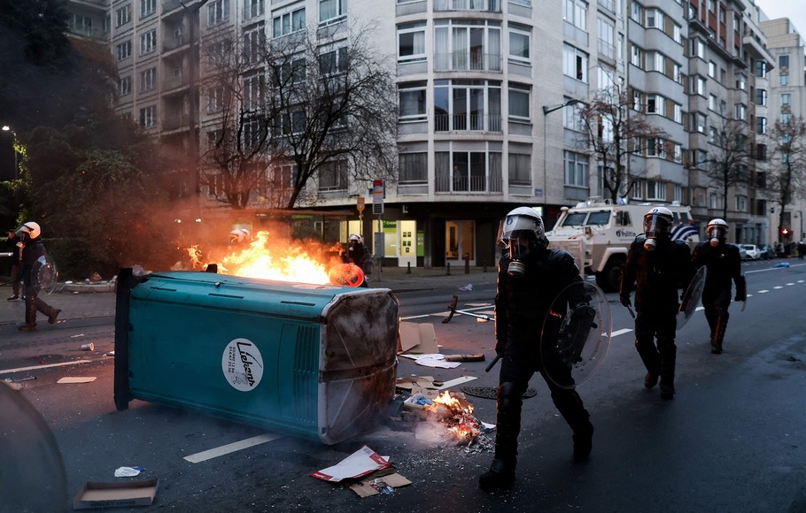 Polisi anti huru hara Belgia berjalan melewati api ketika bentrokan meletus selama demonstrasi menentang aturan Covid-19 dan vaksinasi wajib di Brussels pada 5 Desember 2021.