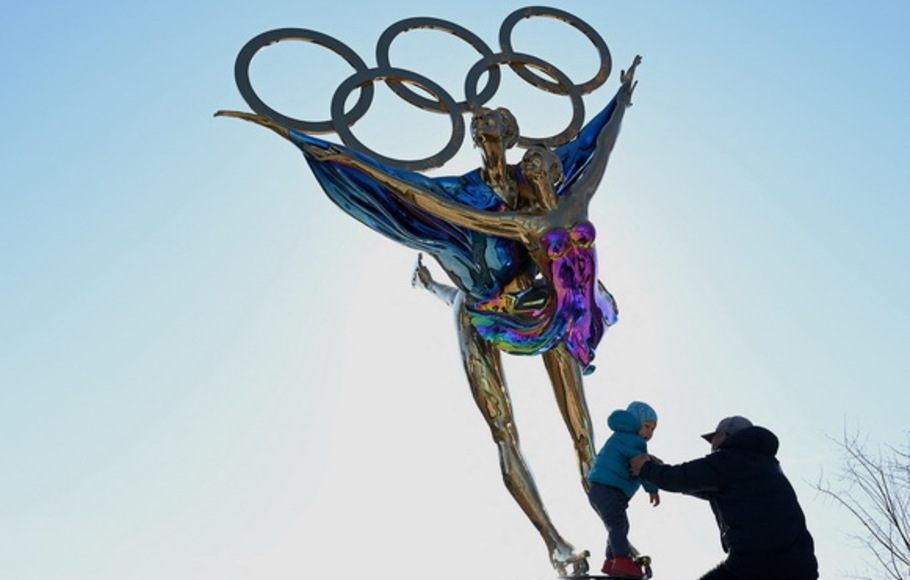 Seorang anak berdiri di atas patung dengan Cincin Olimpiade berjudul 