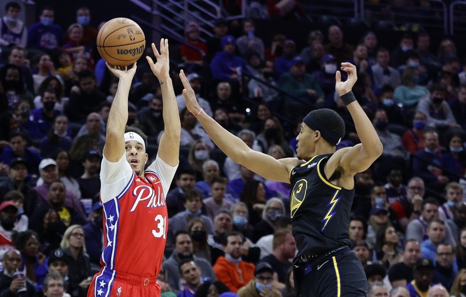 Pemain Philadelphia 76ers Seth Curry melepaskan tembakan yang dijaga pemain  Golden State Warriors Jordan Poole pada pertandingan NBA di Wells Fargo Center di Philadelphia.