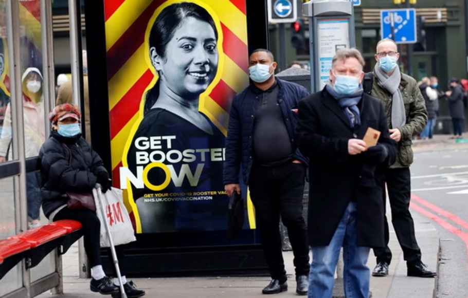 Orang-orang yang mengenakan penutup wajah untuk memerangi penyebaran virus corona menunggu di halte bus yang menampilkan iklan pemerintah yang mempromosikan program vaksin penguat Covid-19 NHS di London, Inggris pada Jumat 17 Desember 2021. 