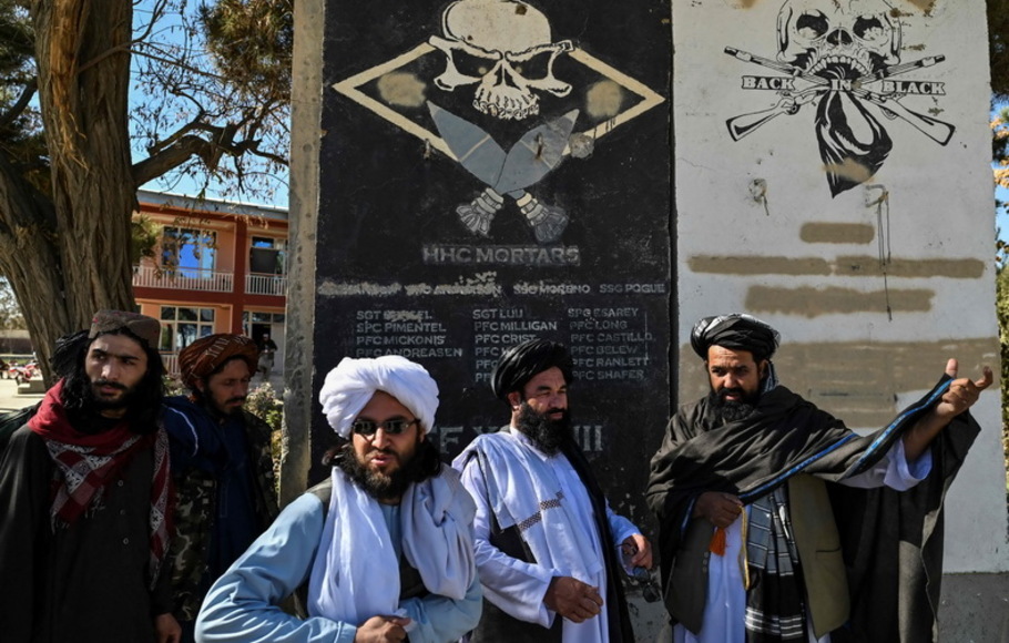 Kepala budaya provinsi Taliban Mullah Habibullah Mujahid (kanan) berdiri dengan anggota Taliban di sebelah bagian dinding bekas pangkalan militer AS dengan nama tentara AS di Ghazni, Afghanistan pada 15 November 2021.