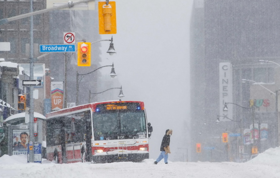 Seorang pejalan kaki menyeberang jalan saat bus kota terjebak saat badai musim dingin di Toronto, Ontario, Kanada, pada Senin 17 Januari 2022. 