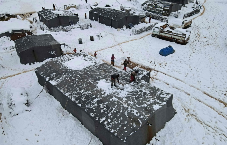 Pemandangan dari udara menunjukkan warga Suriah membersihkan salju di atas tenda mereka di satu kamp untuk pengungsi internal di kota Raju di pedesaan utara yang dikuasai pemberontak di provinsi Aleppo Suriah pada Rabu 19 Januari 2022. 