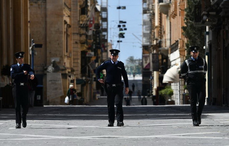 Tiga petugas polisi berjaga di Valletta, Malta, pada 29 Maret 2020 di tengah merebaknya kasus Covid-19.