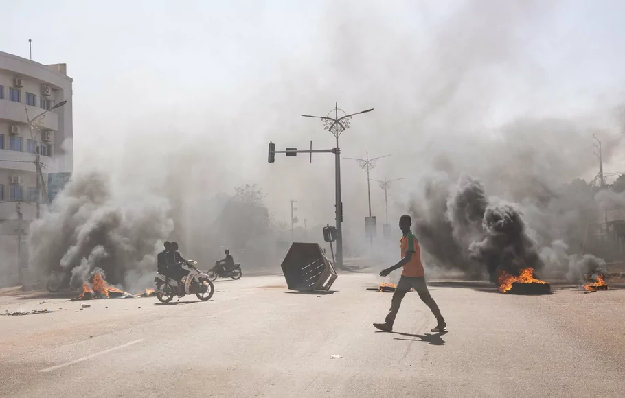 Seorang pria melintasi barikade yang terbakar di jalan utama di Ouagadougou di mana sekelompok demonstran muda yang mendukung peran tentara memprotes Presiden Marc Christian Kabore, Burkina Faso, pada 23 Januari 2022.