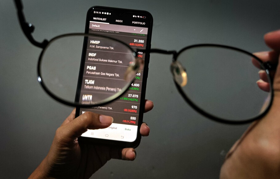 Investor melihat pergerakan harga saham melalui layar ponsel.