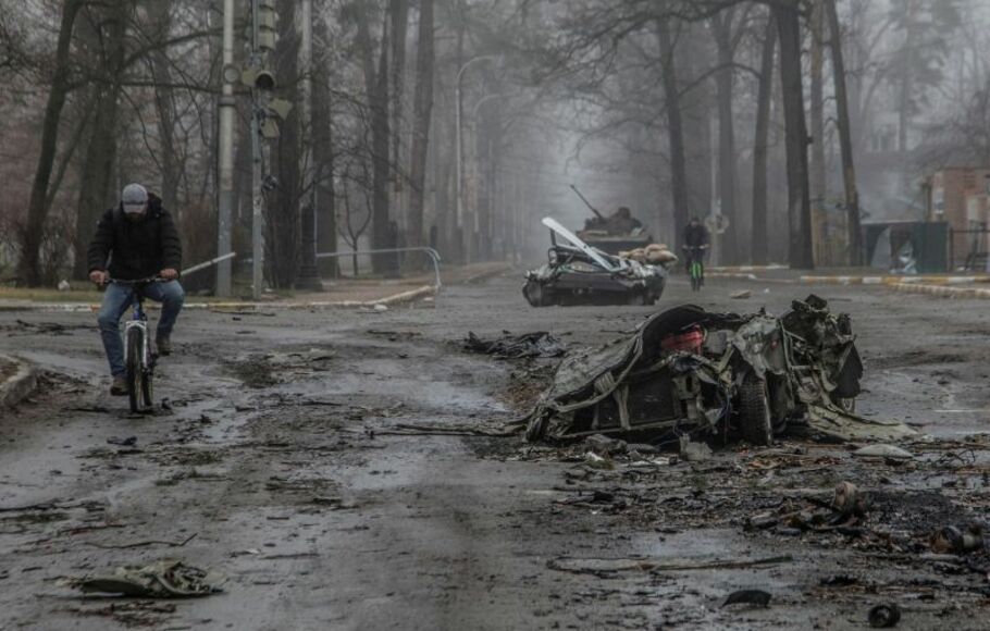 Penduduk mengendarai sepeda melewati mobil warga sipil yang hancur, saat serangan Rusia ke Ukraina di sebuah jalan di kota Bucha, sebelah utara Kyiv.