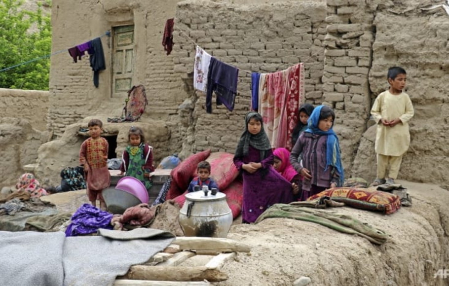 Anak-anak yang terkena banjir bandang duduk di luar rumah mereka yang rusak di distrik Qadis, provinsi Badghis, Afghanistan, pada Rabu 4 Mei 2022.