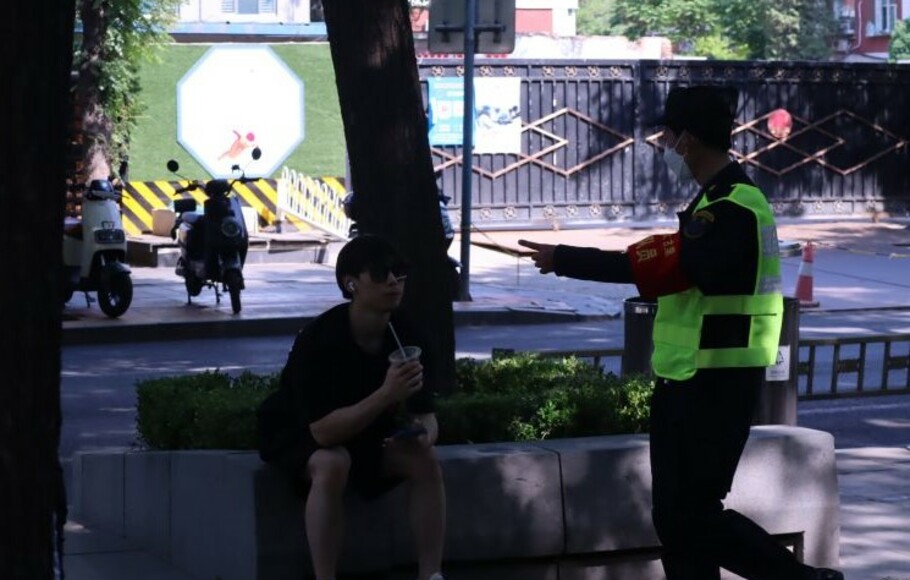 Seorang petugas keamanan mengingatkan warga yang sedang menikmati makanan agar tidak berlama-lama duduk di pinggir jalan di Distrik Chaoyang, Beijing, Tiongkok.