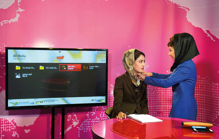 Seorang rekan sejawat merapihkan jilbab presenter sebelum rekaman di stasiun TV Zan di Kabul, Afghanistan. Saluran ini bertujuan untuk menantang ekspektasi tradisional tentang peran perempuan di Afghanistan.