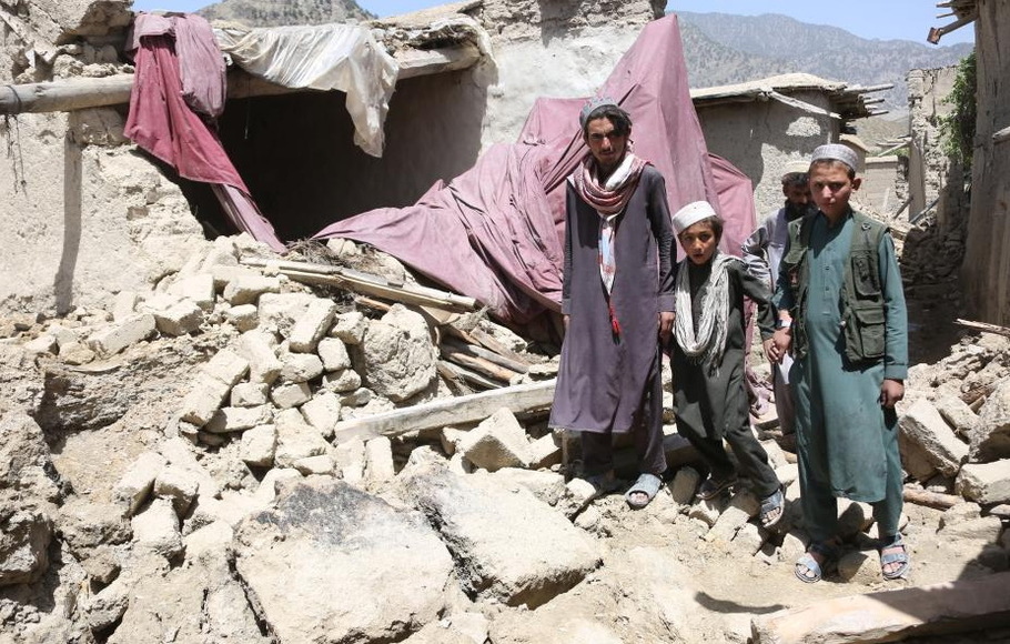 Orang-orang berdiri di atas puing-puing satu rumah yang rusak akibat gempa bumi di provinsi Paktika, Afghanistan, pada Kamis 23 Juni 2022. Pemerintah yang dikelola Taliban di Afghanistan telah meminta bantuan internasional di tengah operasi penyelamatan.