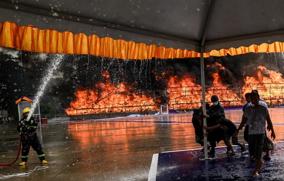 Pekerja memindahkan sebuah tenda di depan tumpukan narkotika yang dibakar di Yangon, Myanmar pada 26 Juni 2022.