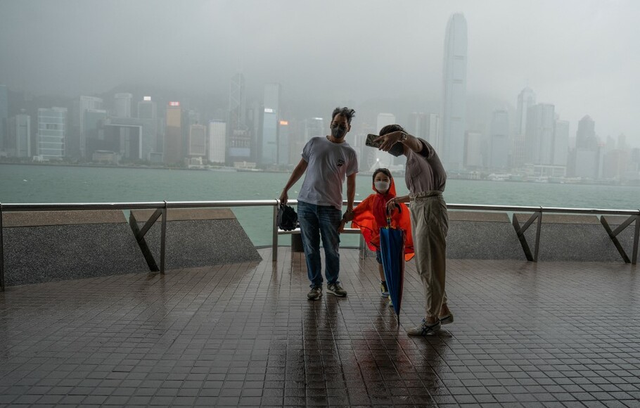 Orang-orang berfoto selfie di tengah hujan lebat di kawasan pejalan kaki di sebelah Pelabuhan Victoria saat Topan Chaba melewati Hong Kong pada 2 Juli 2022.