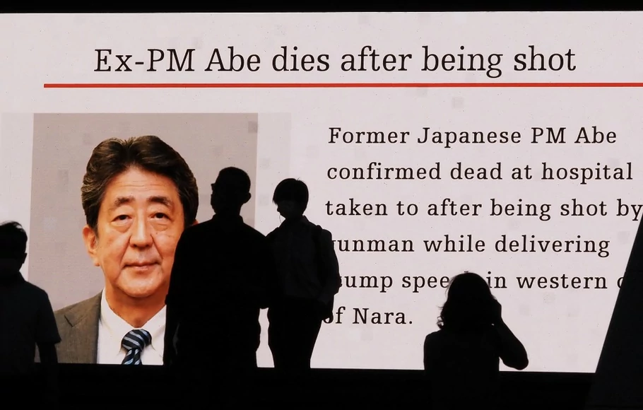 Siluet pejalan kaki di depan layar video publik besar yang menunjukkan gambar mantan perdana menteri Jepang Shinzo Abe di distrik Akihabara Tokyo pada 8 Juli 2022, setelah dia ditembak dan dibunuh di kota Nara.