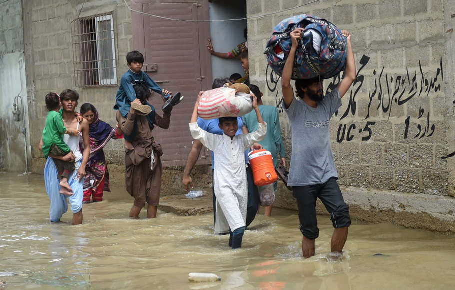Orang-orang membawa barang-barang mereka saat mengarungi jalan yang banjir setelah hujan deras di Karachi, Pakistan pada Senin 11 Juli 2022.