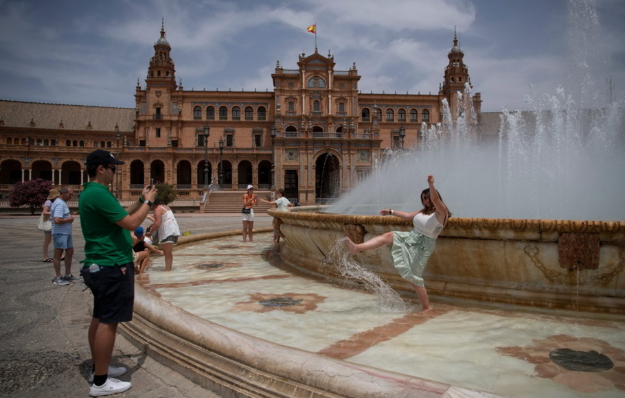 Orang-orang mendinginkan diri dengan air mancur selama gelombang panas di Seville pada Selasa 12 Juli 2022. Petugas pemadam kebakaran berjuang melawan kebakaran hutan di Spanyol dan Portugal saat Eropa Barat menghadapi gelombang panas kedua dalam waktu kurang dari sebulan.
