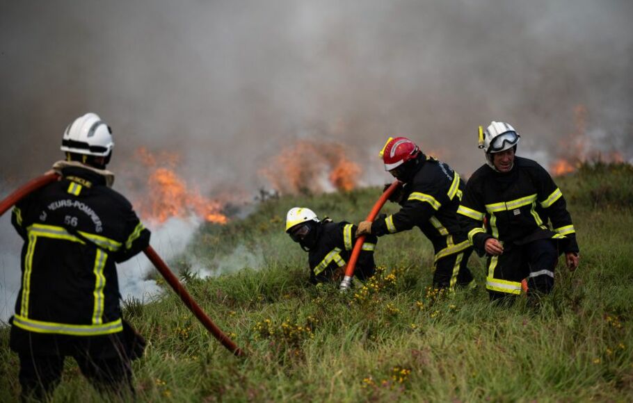 Petugas pemadam kebakaran menyemprotkan air ke api yang berkobar di Monts d'Arree, dekat Brasparts, Brittany, Prancis, pada Selasa 19 Juli 2022.  Gelombang panas yang memicu kebakaran hutan ganas di Eropa mendorong suhu di Inggris lebih dari 40 derajat celsius.
