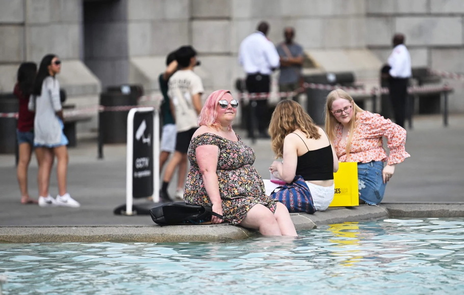 Pejalan kaki mendinginkan diri dengan merendam kaki mereka di air mancur Trafalgar Square di London selama gelombang panas pada Rabu 13 Juli 2022. 