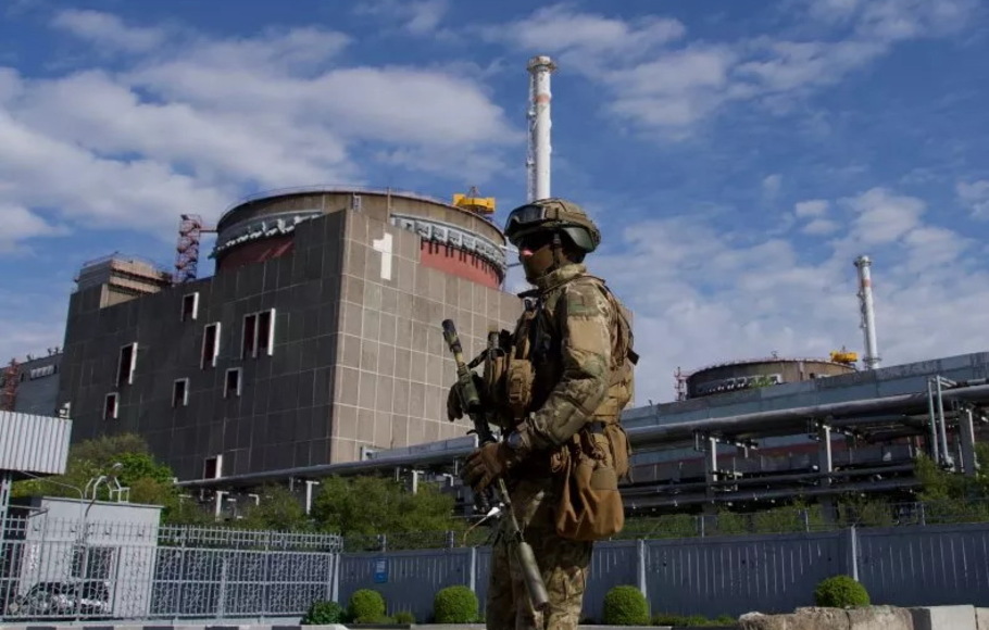 Seorang prajurit Rusia berpatroli di sekitar pabrik di Enerhodar, Ukraina, pada 1 Mei 2022. Ukraina menyatakan bahwa serangan Rusia terhadap pembangkit listrik tenaga nuklir Zaporizhzhia bisa disamakan dengan 