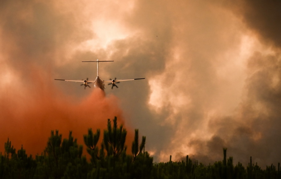 Pesawat pemadam kebakaran menyemprotkan bahan tahan api di atas pohon selama kebakaran hutan di dekat Belin-Beliet di Gironde, Prancis barat daya, pada Rabu 10 Agustus 2022. 
