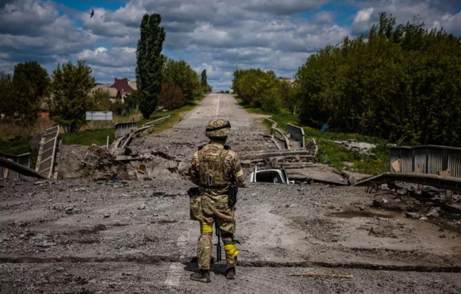 Seorang prajurit unit pasukan khusus Ukraina Kraken mengamati area di jembatan yang hancur di jalan dekat desa Rus'ka Lozova, utara Kharkiv, pada 16 Mei 2022. Ukraina telah menargetkan Jembatan Antonovsky beberapa kali menggunakan senjata presisi tinggi HIMARS yang dipasok AS.