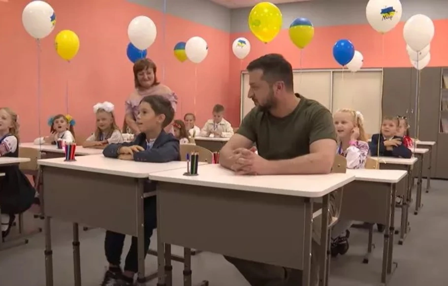 Presiden Ukraina Volodymyr Zelensky duduk di meja sekolah bersama anak-anak di Irpin, Ukraina, pada Kamis, 1 September 2022. Zelensky mengunjungi sekolah Irpin yang dibangun kembali dan memberi selamat kepada siswa kelas satu dan guru mereka pada Hari Pengetahuan.