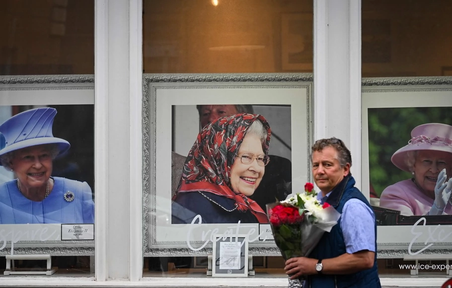 Seorang pria yang membawa buket bunga berjalan melewati foto Ratu Elizabeth II dari Inggris di luar Kastil Windsor, barat London, pada Selasa 13 September 2022, setelah kematiannya pada 8 September. 